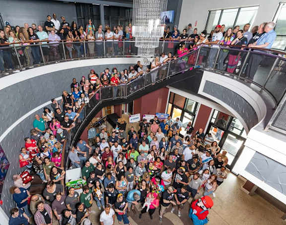 A large group of people are gathered in a circular formation in a building with a glass ceiling.