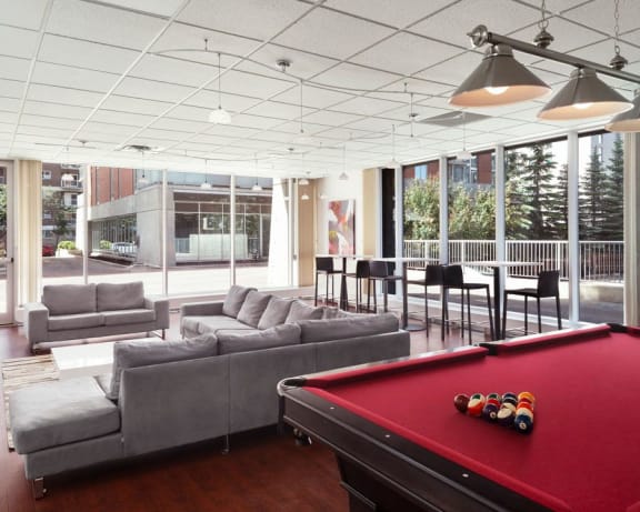 social room with a pool table, couches and several stools looking out a large window