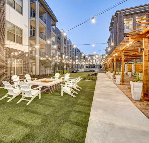 A patio with white chairs and a table is surrounded by apartment buildings at Arise Riverside Apartments, Austin, TX, 78741