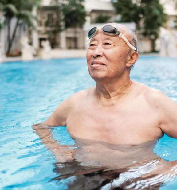 A man is sitting in a pool with goggles on his head.