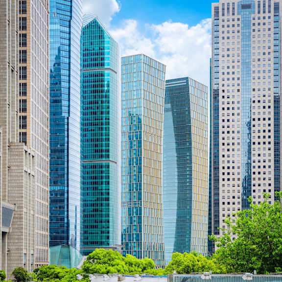 A cityscape with tall buildings and greenery in the foreground.