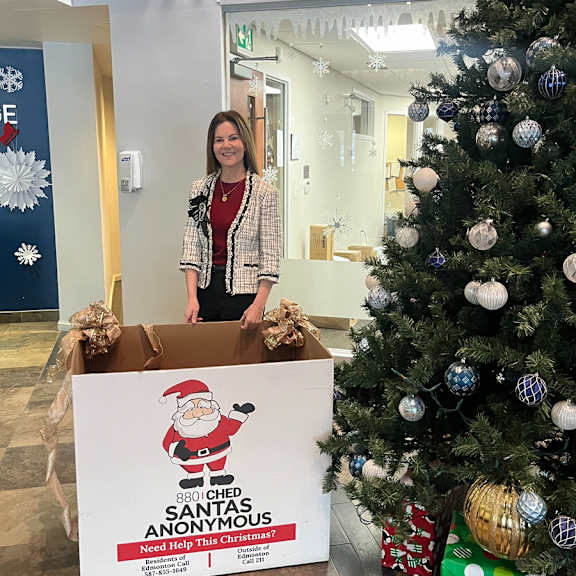 A woman standing next to a Christmas tree and a box with a Santa Claus picture on it.