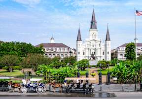A horse-drawn carriage is parked in front of a large white building with two towers.