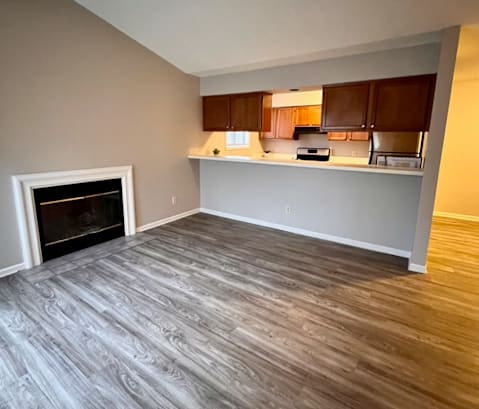 an empty living room with a fireplace and a kitchen in the background