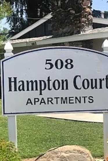 A sign for Hampton Court Apartments stands in front of a house.