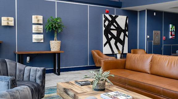 A living room with a grey sofa, a brown leather sofa, a wooden coffee table, and a potted plant at Aqua Via Apartments, Oakland, CA