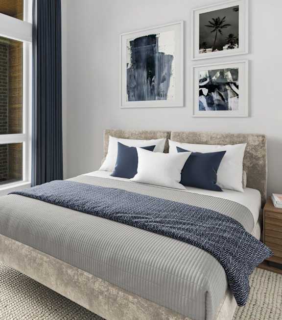 A bed with a grey and blue comforter and pillows in a room with artwork on the wall.