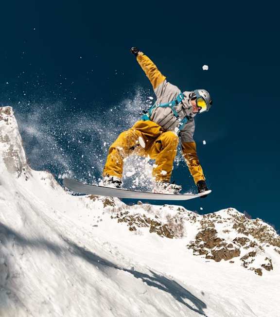 A snowboarder in yellow pants and a grey jacket is performing a trick on a snowy mountain.