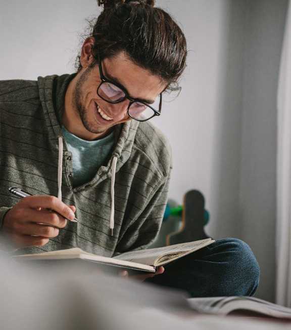 A person with glasses is writing in a notebook.
