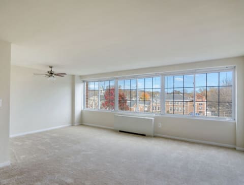 an empty living room with a ceiling fan and large windows