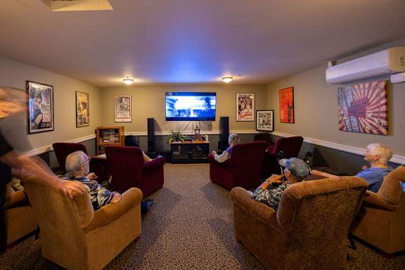 A group of elderly people are sitting in a room with a television and a fireplace.