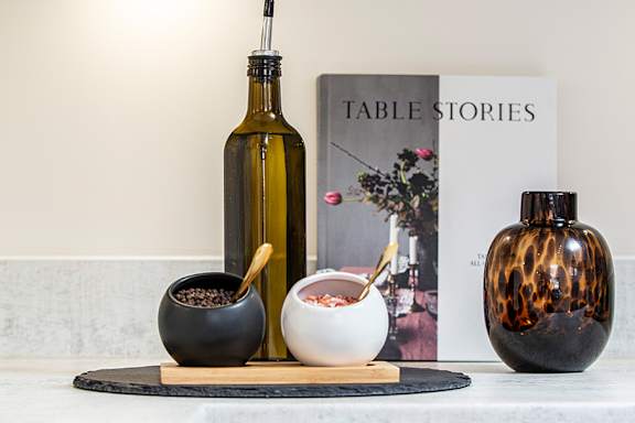 A book titled "Table Stories" is on a table next to a bottle of wine and two bowls of food.