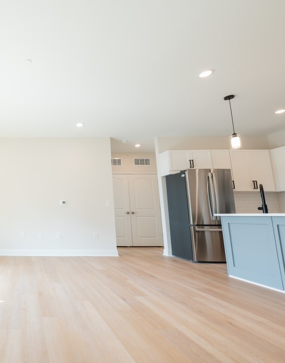 an empty living room with a large window and a stainless steel refrigerator