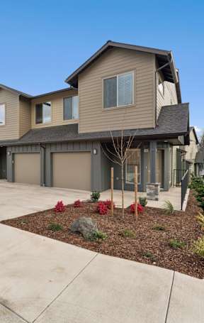 A house with a brown siding and a grey roof with a driveway in front.