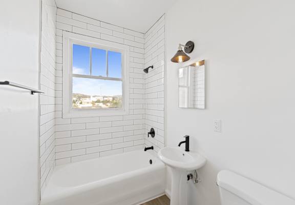 A white bathroom with a tub, sink, and window.