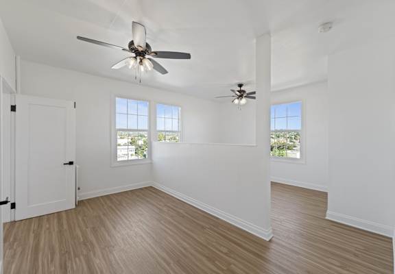 A room with a ceiling fan and two windows.