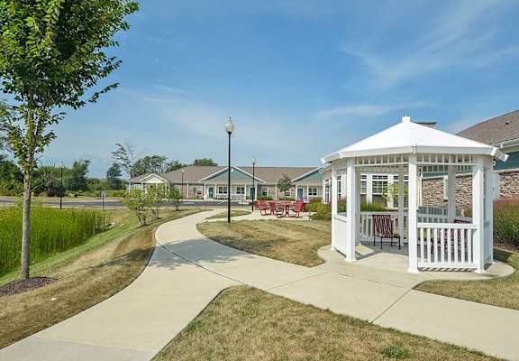 A white gazebo is surrounded by a paved walkway in a grassy area.