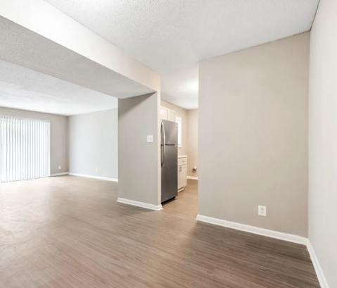 an empty living room with wood flooring and a stainless steel refrigerator