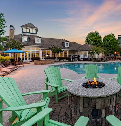 A fire pit surrounded by green chairs sits in the middle of a pool area.