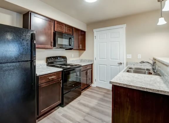 A kitchen with a black refrigerator, brown cabinets, and a white door.