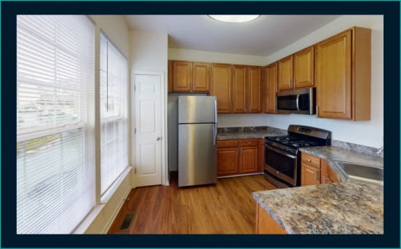 a kitchen with wooden cabinets and a stainless steel refrigerator at Townes at Village Center Apartments, Reisterstown, 21136