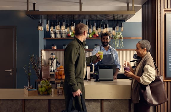 A man in a green sweater is standing at a bar with a bartender.