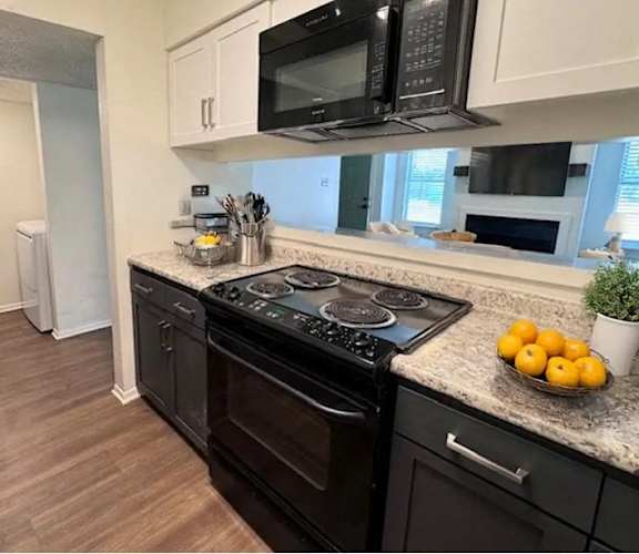 A black stove top oven sits in a kitchen with black appliances and white cabinets.