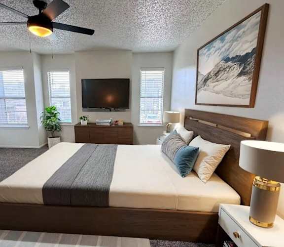 A bedroom with a large bed, a flat screen TV, and a ceiling fan.