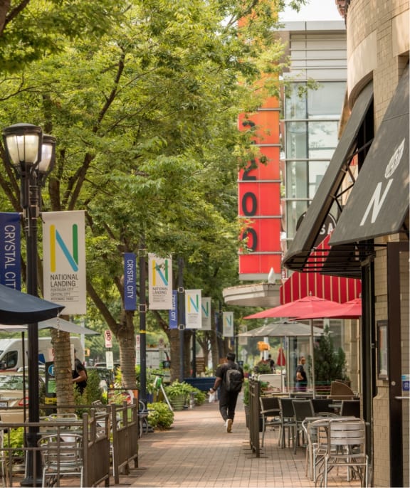a city street with cafes and trees and a person walking down the sidewalk