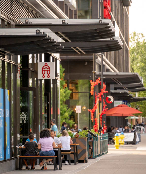 people sitting at tables outside of a restaurant on a city street
