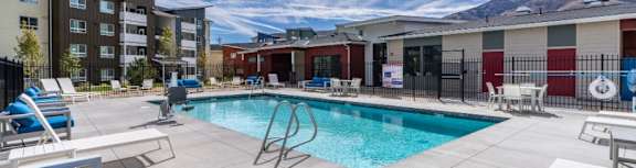 A swimming pool surrounded by lounge chairs and buildings in the background.