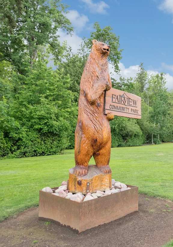 A bear statue stands in front of a sign that says Fairview Community Park. at Fairview Village Apartments, Fairview, Oregon