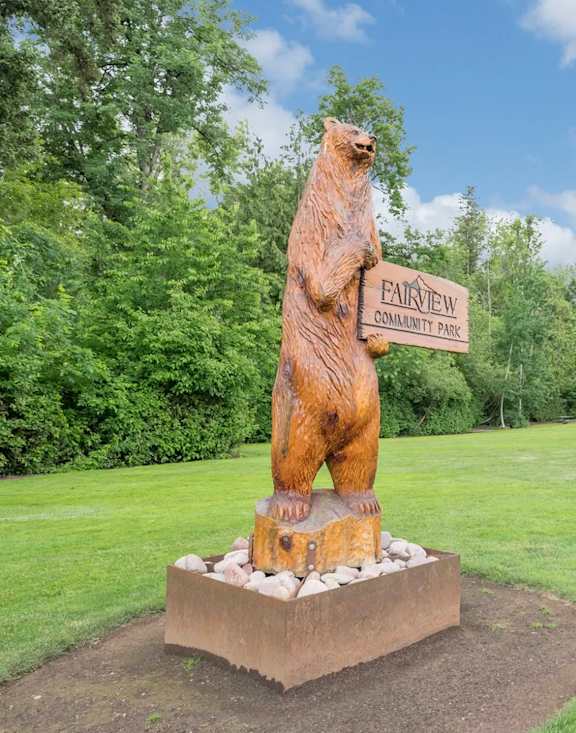 A bear statue stands in front of a sign that says Fairview Community Park. at Fairview Village Apartments, Fairview, Oregon
