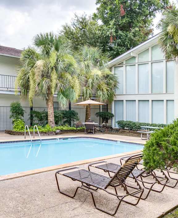 A pool surrounded by a patio with chairs and a table.