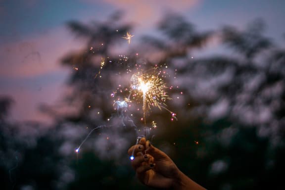Hand holding sparkler against backdrop of sky and trees at Mirabella Apartments, California, 92203