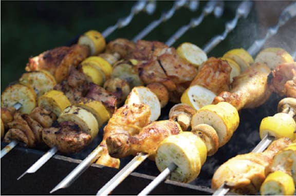 a barbecue grill with skewers of chicken skewers and potatoes