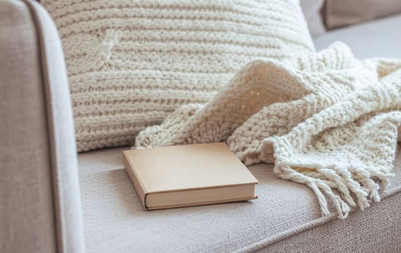 A white knitted pillow with a book on a couch.