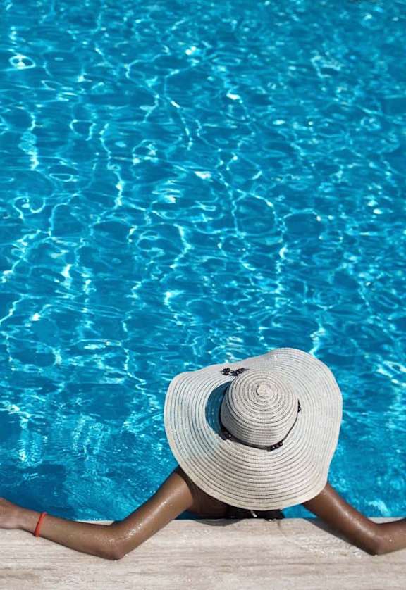 a woman laying on the side of a pool with a hat