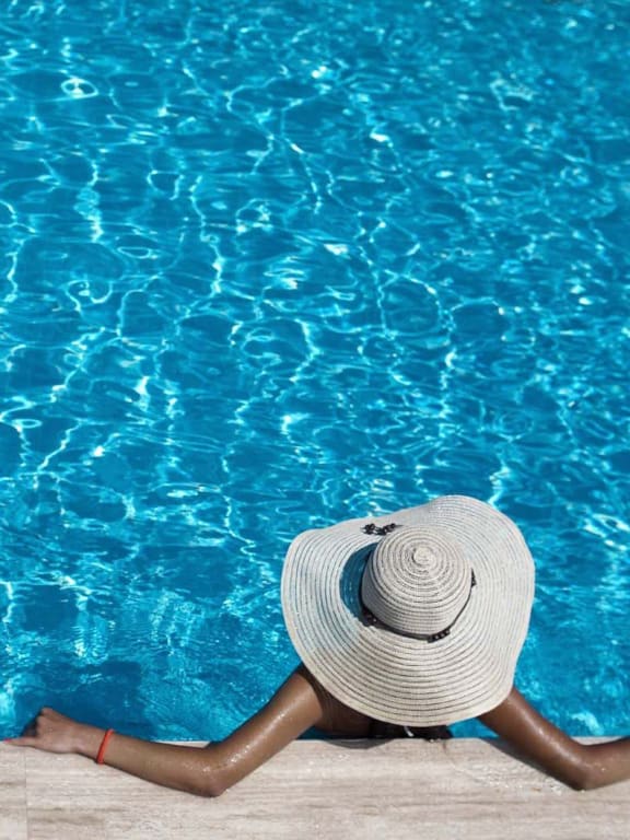 a woman laying on the side of a pool with a hat