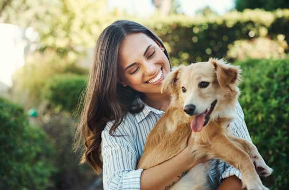 A woman is hugging a happy dog in a sunny outdoor setting.