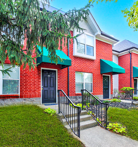 A red brick house with a black door and a green awning.