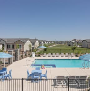 A pool area with blue chairs and umbrellas in front of a row of houses.