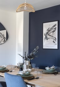a dining room with a wooden table and blue chairs and a blue wall with artwork
