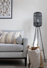 a living room with a couch and a black tripod lamp