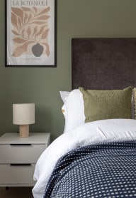 a bedroom with a bed and a nightstand with a lamp and a framed picture