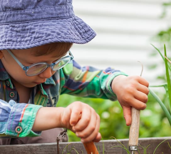 a little boy in a hat and glasses is planting a carrot in the garden