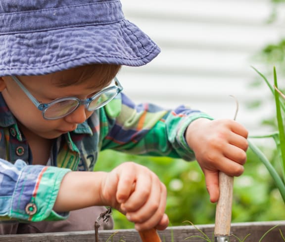 a little boy in a hat and glasses is planting a carrot in the garden