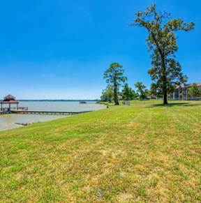 A grassy field with a dock that leads above the water on a bridge to a covering