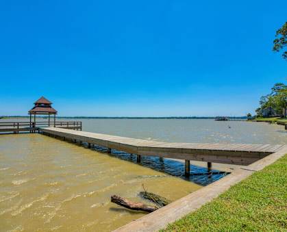 A grassy field with a dock that leads above the water on a bridge to a covering