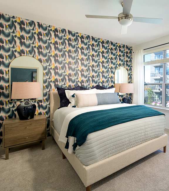 A bedroom with a bed, nightstand, and a wallpapered wall.